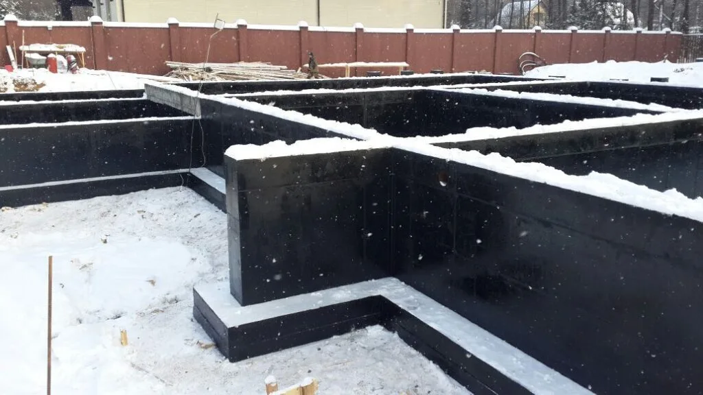 Фундамент загородного дома из бетона с гидроизоляцией на зимней стройплощадке в снегу