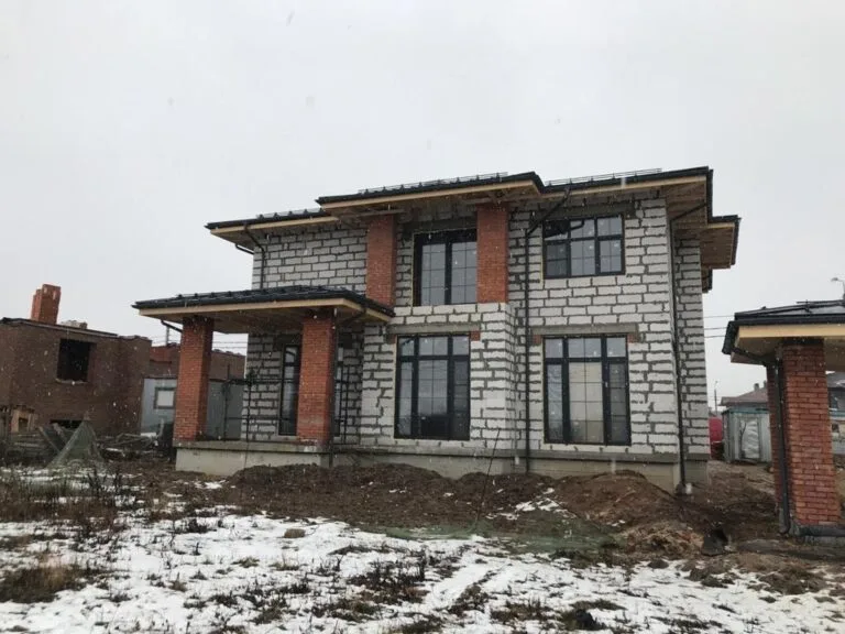 Двухэтажный дом из газобетона с кирпичными колоннами на этапе внешней отделки зимой